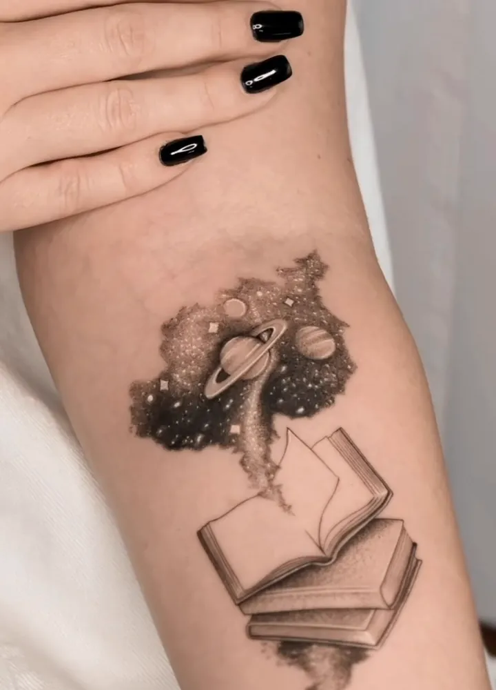 Livros abertos com um universo de planetas saindo das páginas, cobrindo uma tatuagem antiga
