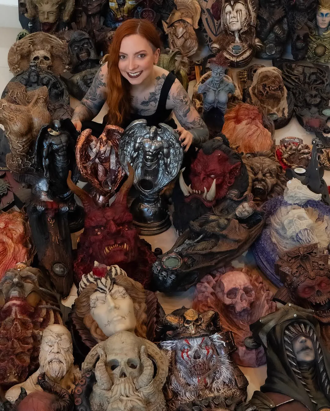 Fran Dubiel sorrindo, sentada no meio de dezenas de troféus de convenções de tatuagem